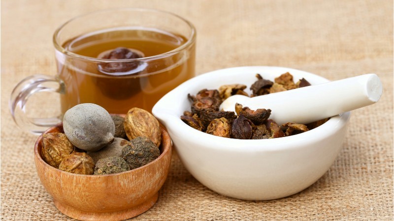 ajurwedyjskie suszone owoce triphala w miseczce i moździerzu oraz szklanka z napojem triphala